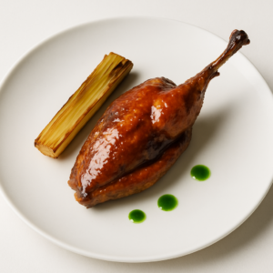 Perlhuhn mit glänzender Miso-Vanille-Glasur auf weißem Teller mit gebratenem Lauch und grünem Kräuteröl.