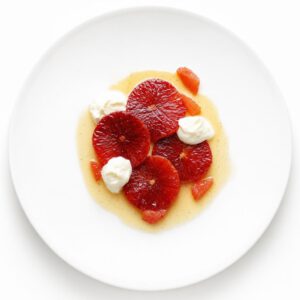 Pochierte Blutorangenscheiben mit Vanille-Beurre-blanc und Joghurtcreme auf einem weißen Teller