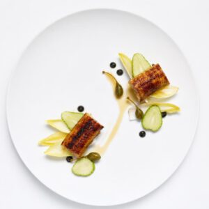 Geflämmter Aal mit grüner Erdbeere, schwarzem Knoblauch und Kapernknospen auf einem weißen Teller