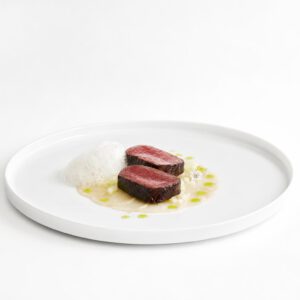 Zentriert angerichtetes lackiertes Wagyu mit schwarzer Knoblauchglasur, Kohlrabi und heller Molkenluft auf weißem Teller.