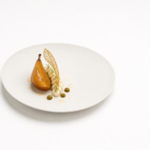 Ofenbirne mit aufgeschlagener Estragoncrème, Oliven-Haselnuss-Praliné und Fenchelhippe auf einem weißen Teller