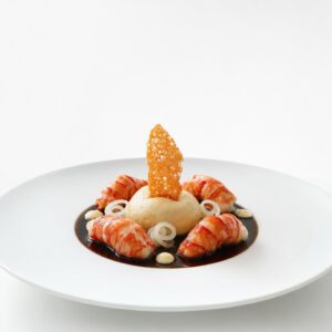 Rote Garnele mit heller Mousseline, Yuzu-Daikon, dunklem Krustentierjus und knusprigem Reisblatt auf weißem Teller